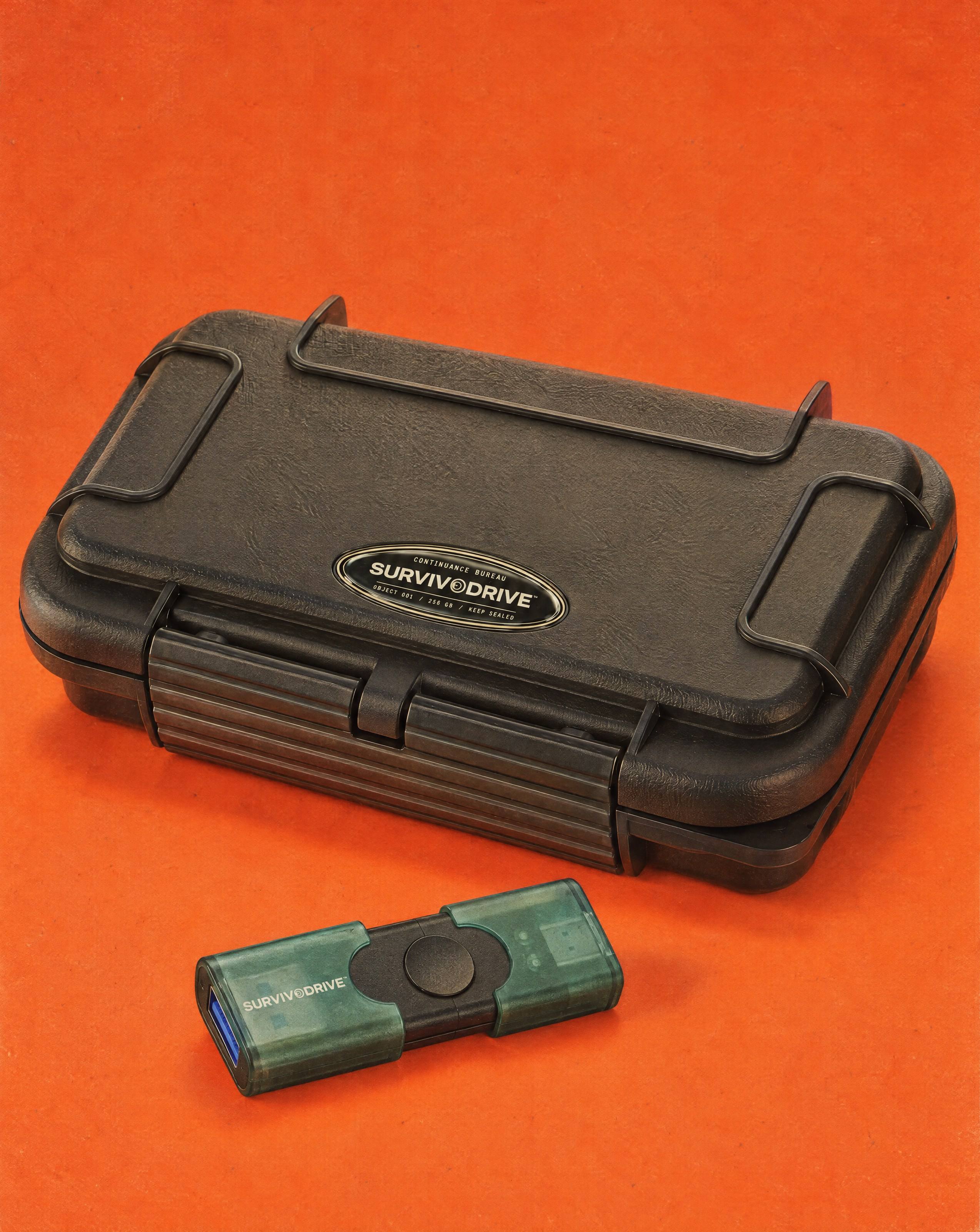 The SURVIVODRIVE case at a three-quarter angle on a signal-orange backdrop, the green dual USB drive lying in front of it