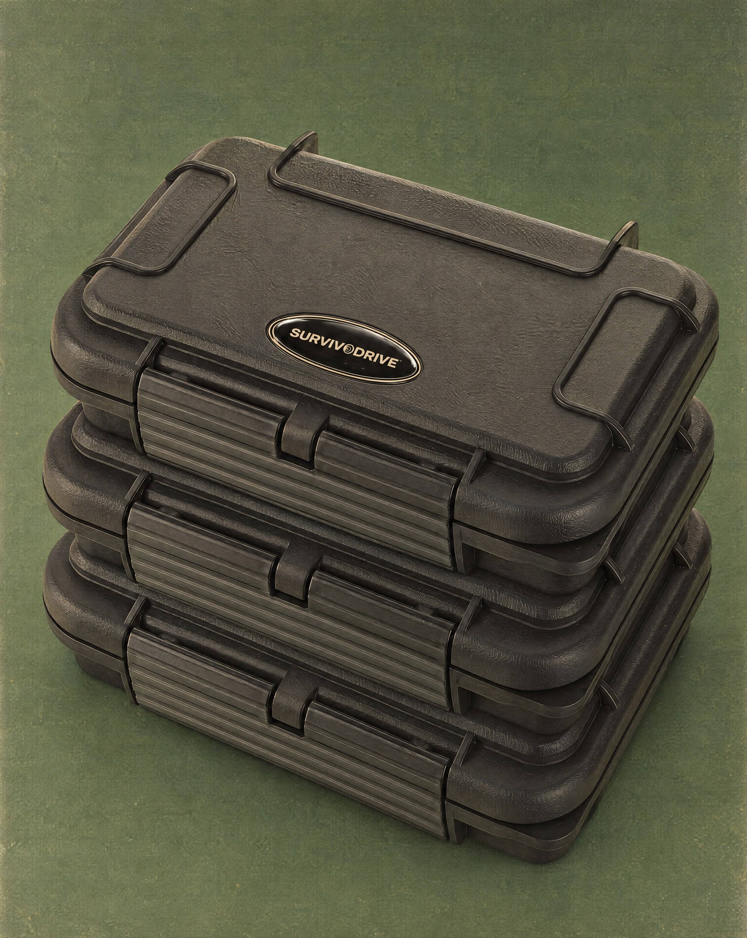 Three SURVIVODRIVE cases stacked flat against a deep green backdrop, the domed badge on the top lid